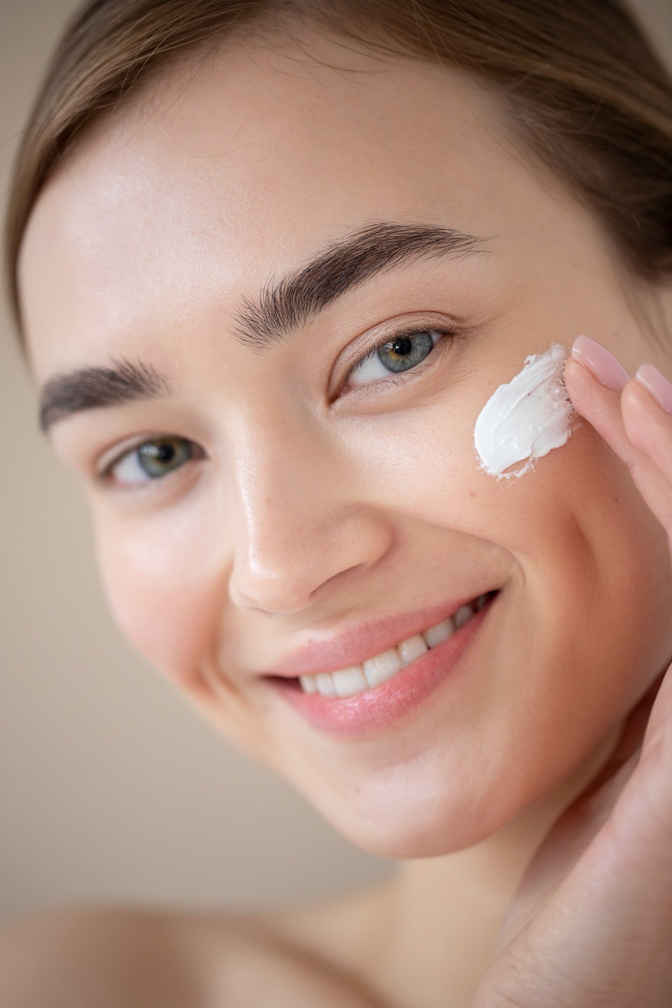 Femme souriante appliquant une crème hydratante visage naturelle sur sa joue