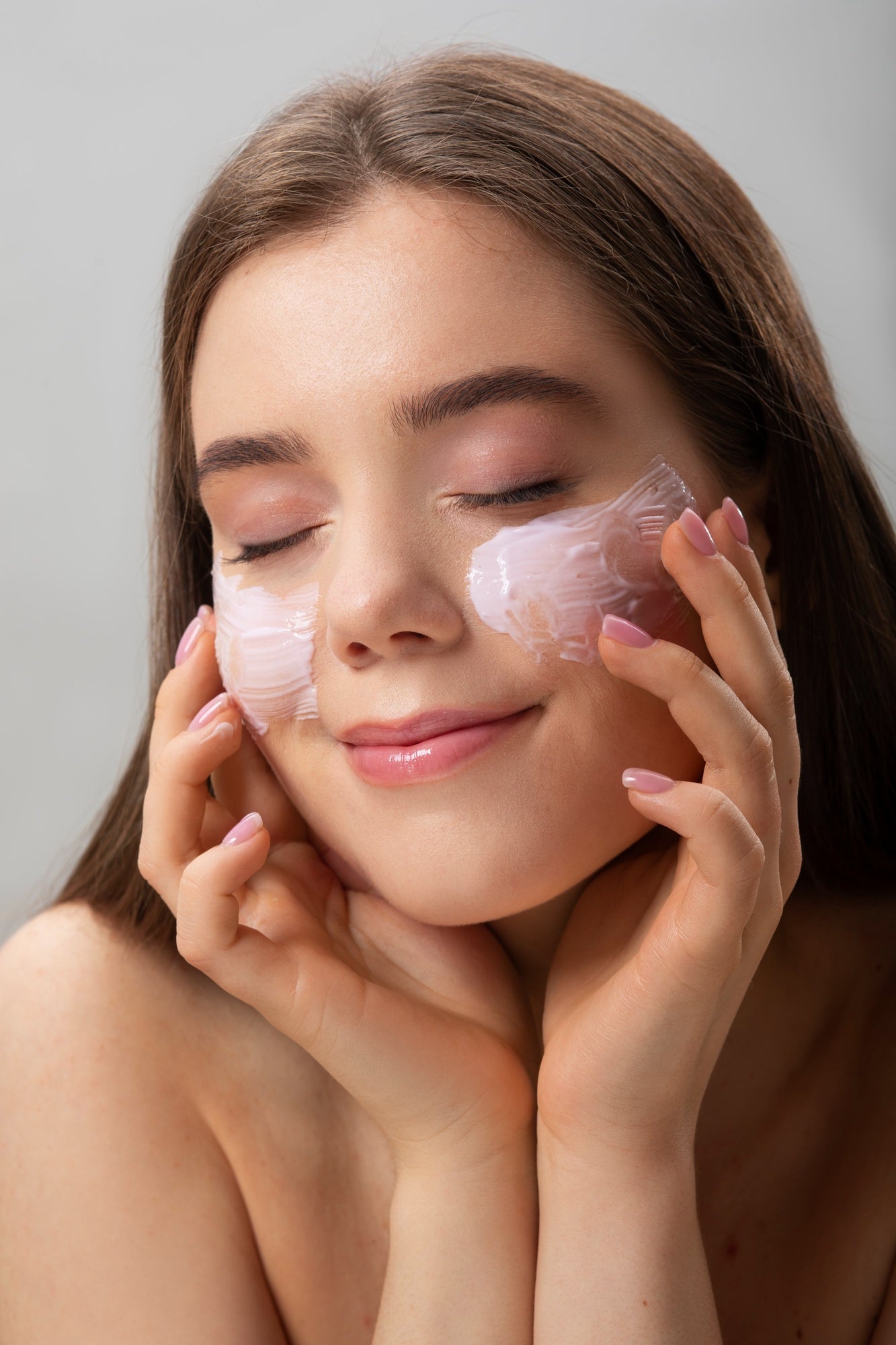 Femme détendue appliquant une crème hydratante visage sur ses joues, les yeux fermés
