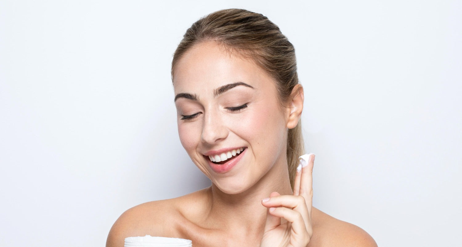 Femme souriante appliquant une crème hydratante sur son visage pour une peau douce et éclatante.